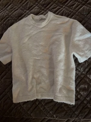 Vit stickad topp från Gina Tricot - Säljer en vit stickad t-shirt från Gina Tricot med korta ärmar och ribbad rund halsringning. Materialet är mjukt och har en lätt struktur, perfekt för att skapa en clean och stilren look. Passar dig som gillar enkel och modern design. Använd men i fint skick 