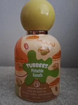 Tubbees Pistachio Kunafa parfym - Tubbees Pistachio Kunafa Eau de Parfum från Grandeur har en unik och lekfull design med pistagegrön splash och bakverksmotiv på flaskan. Flaskan är rund med en ljusgrön bollformad kork och rymmer 50 ml. Perfekt för dig som gillar söta och kreativa dofter.