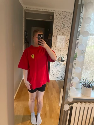 Röd Ferrari t-shirt oversized - Säljer en röd oversized t-shirt från Ferrari med klassisk logga på bröstet. T-shirten har korta ärmar och rund halsringning