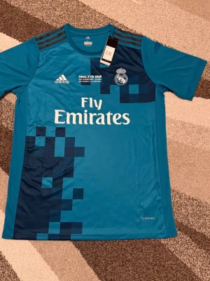 Real Madrid 17-18 Tredjetröja  - Säljs av ICEKIT  Storlek: L Namn + nummer: Ronaldo #7 Badge: Ingen  Här kan du se tröjor i ICEKIT Outlet. Alla tröjor är helt nya och utan några problem. Du kan välja att köpa dem här eller direkt via vår hemsida.  Tröjorna finns tillgängliga hos ICEKIT på: https://www.icekit.se  Länk: https://www.icekit.se/collections/outlet