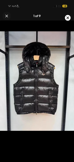 Svart dunväst med huva från Moncler - Snygg svart dunväst från Moncler med glansig finish och avtagbar huva. Västen har två dragkedjefickor framtill och en diskret Moncler-logga på bröstet. Perfekt för lager-på-lager och håller dig varm under kyliga dagar.