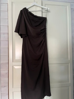 Mörkbrun one shoulder långklänning - Snygg mörkbrun långklänning med one shoulder, helt ny med prislapp kvar endast provad 2 gånger! 