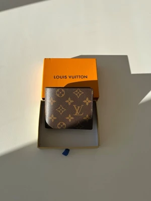 Kouis Buitton monogram plånbok - Snygg brun plånbok från Kouis Buitton med klassiskt monogrammönster i guld. Tillverkad i tåligt läder med flera kortfack och stilren design. Perfekt accessoar för dig som gillar lyxiga detaljer och tidlös stil. Helt ny oanvänd skick 10/10. Vid frågor är det bara att säga till Mvh Olof.