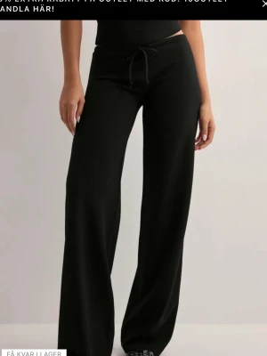 Low waist crepe pants nelly💕 - Svarta mjukisbyxor med bred passform och dragsko i midjan. Byxorna har raka ben och är tillverkade i ett mjukt och stretchigt material som känns skönt mot huden. Perfekta för en avslappnad och trendig look.