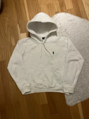 Vit Ralph Lauren Hoodie  - Vit Ralph Lauren Hoodie 🤩 Marinblå logotypfärg (Den ser svart ut på bilderna men den är marinblå och tydligare med riktiga ögon) Storlek: M för DAM, passar ungefär XS-S för HERR 👔 Färg: Vit ⚪️ Skick: Mycket bra, nästan inga tecken på användning! 🌟 Jag rekommenderar att du köper!