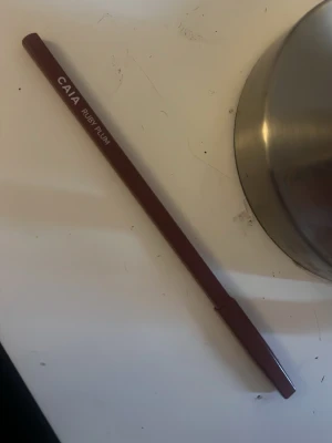 CAIA Ruby Plum läppenna - Snygg läppenna från CAIA i färgen Ruby Plum. Pennan har en djup plommonröd ton och klassisk smal form med lock. Perfekt för att definiera och fylla i läpparna med precision. Tillverkad i trä med mjuk formula som glider lätt på läpparna.