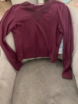 Vinröd långärmad topp med spets - Säljer en vinröd långärmad topp med vacker spetsdetalj vid halsringningen. Tröjan har en smal passform och är tillverkad i ett mjukt, stretchigt material. Perfekt för dig som gillar stilrena plagg med en twist.