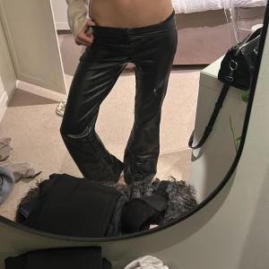 Svarta skinnbyxor  - Säljer ett par svarta byxor i skinnimitation låg midja. Byxorna har klassiska bakfickor och en snygg glansig finish som ger en edgy vibe. Perfekta för dig som vill sticka ut med en cool look.