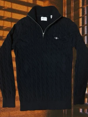 Mörkblå kabelstickad tröja Gant - Kabelstickad mörkblå tröja från Gant med halv dragkedja och hög krage. Tröjan har ribbade muddar och diskret Gant-logga broderad på bröstet. Perfekt för lager på lager och klassisk stil.