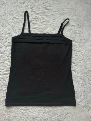 Svart linnetopp med smala axelband - En enkel och stilren svart linnetopp med smala axelband och diskreta ribbade detaljer upptill.