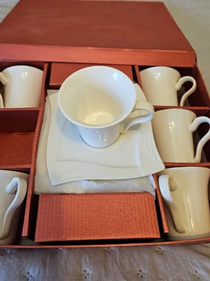 Vitt kaffekoppset i porslin - Säljer ett elegant set med sex vita kaffekoppar och tillhörande fyrkantiga fat i porslin. Kopparna har klassisk form med rundad kant och bekvämt handtag. Allt levereras i en snygg röd presentförpackning, perfekt för fika eller som present.