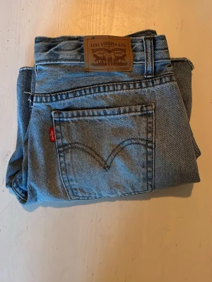 Levi's ljusblå raka jeans - Klassiska ljusblå jeans från Levi's med rak passform och femficksmodell. Jeansen har den ikoniska röda Levi's-lappen på bakfickan och läderpatch i midjan. Tillverkade i slitstark denim, perfekta för en avslappnad och tidlös stil.
