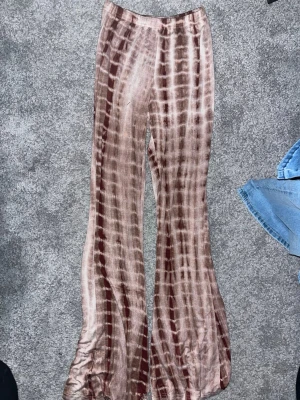 Bruna batikmönstrade leggings - Säljer ett par bruna leggings med batikmönster och utsvängda ben. Materialet är stretchigt och mjukt, vilket gör dem riktigt bekväma. Perfekta för dig som gillar en avslappnad och trendig stil.