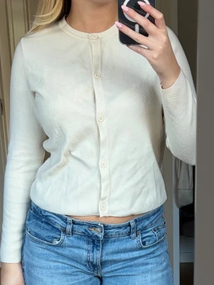 Krämvit ribbad kofta med rund hals - Säljer en krämvit ribbad kofta med rund halsringning och långa ärmar. Koftan har knäppning framtill med matchande knappar och är i ett mjukt, tunt material som sitter snyggt🫶🏼