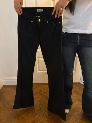 Svarta bootcut jeans - Säljer ett par svarta bootcut jeans med klassisk femficksdesign och silverfärgade knappar. Jeansen har en snygg utsvängd passform nedtill och är perfekta för en trendig look.💕 manchester tyg, prislappen är kvar 