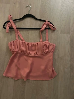 Rosa linnetopp med knyt från Zara - Supersöt rosa linnetopp från Zara med knytbara axelband och rynkad överdel. Toppen har en luftig passform och är perfekt för varma dagar. Tillverkad i ett mjukt och lätt material som känns skönt mot huden.