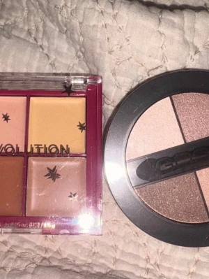 Ögonskuggspaletter i nude och brunt - Två ögonskuggspaletter, en fyrkantig från Revolution med fyra nyanser i nude, beige och brunt samt en rund palett med tre skimrande toner i rosa, champagne och brons. Perfekta för att skapa naturliga eller sotade ögonlooks. Plastförpackningar med genomskinliga lock.