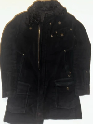 Svart J lindeberg Jacka - Svart vadderad parkajacka i manchestertyg med dragkedja framtill och flera fickor med knappar. Klassisk rak modell med lång ärm och stilrena detaljer. Perfekt för dig som gillar en tidlös och snygg parkas. Saknar en knapp och dragkedjan är lite trög. Nypris cirka 2500-3000, hittar inte exact nypris pga att det är vintage jacka