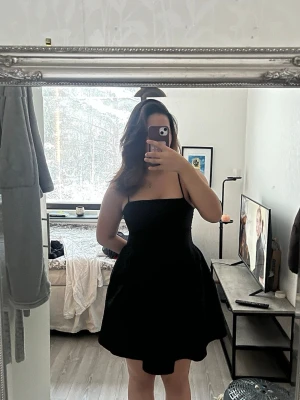 Svart kort klänning från H&M - Supersnygg svart klänning från H&M med smala axelband och markerad midja. Klänningen är kort och har en enkel, stilren design med lätt utställd kjol. Perfekt för dig som gillar minimalistisk stil och vill ha något som känns både trendigt och klassiskt. Endast använd en gång och har även fickor i sig. 