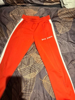 Röda Palm Angels Pants - Säljer ett par röda Palm Angels byxor! Stilrena och mycket bra skick! Priset är 800kr och storleken på byxorna är S. Byxorna är äkta givetvis!🌟