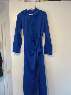 Kornblå lång morgonrock med skärp - Snygg och enkel kornblå morgonrock med lång ärm och knytband i midjan. Modellen är lång och har en klassisk krage. Perfekt för att chilla hemma i. Materialet känns mjukt och följsamt mot huden.