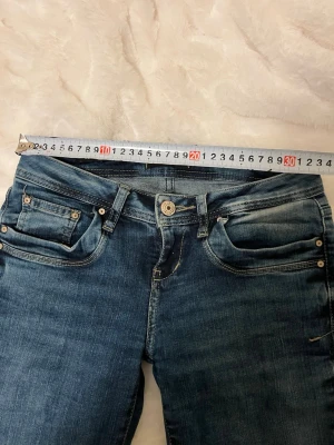 LTB jeans valerie - Snygga blå jeans från LTB med klassisk femficksdesign och lätt slitna detaljer. Jeansen har låg midja, dragkedjegylf och silverfärgade nitar. Perfekta för en trendig och avslappnad look.