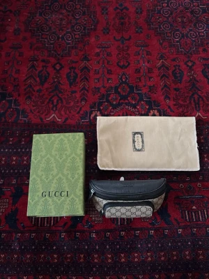 Gucci GG Supreme shoppingväska - Säljer en snygg shoppingväska från Gucci i GG Supreme-mönster. Väskan är beige med svarta detaljer och har ett klassiskt GG-tryck över hela ytan. Kommer med original dustbag och box. Perfekt för dig som vill ha något stilrent och lyxigt i vardagen.