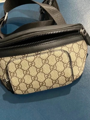 Gucci beige shoppingväska med GG-mönster - Snygg shoppingväska från Gucci i beige canvas med klassiskt GG-mönster och svarta läderdetaljer. Väskan har en framficka med dragkedja och justerbar axelrem i svart textil. Perfekt för dig som gillar lyxiga accessoarer med ikonisk design. Kan skicka fler bilder ifall du är intresserad!