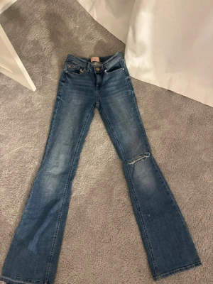 Blå flared jeans från Vero Moda - Säljer ett par blå flared jeans från Vero Moda i modellen VMFLASH MR FLARED. Jeansen har ett snygg hål på ena benet på knät 