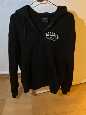 Hoodrich zip hoodie knappt använd  - Säljer en svart hoodie med dragkedja från Hoodrich. Tryck med texten 'HOODRICH EST. 2014 WELCOME TO THE FAMILY' på bröstet och ryggen. Klassisk huva och fickor framtill. Perfekt för en streetwear-look.