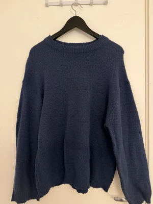 Mörkblå oversized stickad tröja - Mysig mörkblå stickad tröja med avslappnad, oversized passform och rund halsringning. Tröjan har långa ärmar och ribbade muddar vid hals, ärmslut och nederkant. Perfekt för lager på lager och chill stil.