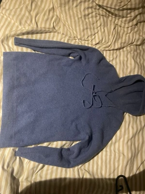 Ljusblå Kashmir hoodie - Mysig blå kashmir hoodie med huva. Tröjan har långa ärmar och ribbade muddar vid ärmslut och nederkant. Perfekt för en avslappnad och stilren look.
