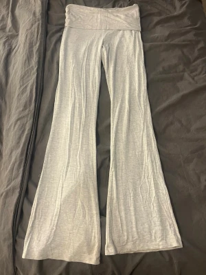 Grå mjukisbyxor med utsvängda ben - Säljer ett par ljusgrå yogapants med bred linning och utsvängda ben. Byxorna är tillverkade i ett mjukt och stretchigt material som känns skönt mot huden. Perfekta för en avslappnad och chill stil. Lite slitna nere vid benen annars väldigt fint skick