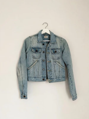 Jeansjacka – Made in the Shade – XS - Jeansjacka i fin ljus tvätt från Made in the Shade, storlek XS. Den har fabriksslitage på axlar och ärmar som alltså fanns där vid inköp (se bilder). Fint skick!