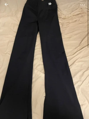 Blåa vida kostymbyxor - Säljer ett par blåa yogabygor med låg midja och vida ben. Byxorna har klassisk passform och stängs med knapp och dragkedja. Perfekta för en stilren look och passar till många olika outfits.