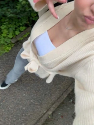 Beige stickad omlottkofta med knytband - Säljer en beige stickad omlottkofta med breda ärmar och knytband i midjan. Koftan har ribbad struktur och en avslappnad passform, perfekt att slänga över en topp. Enkel och stilren design som passar till det mesta.