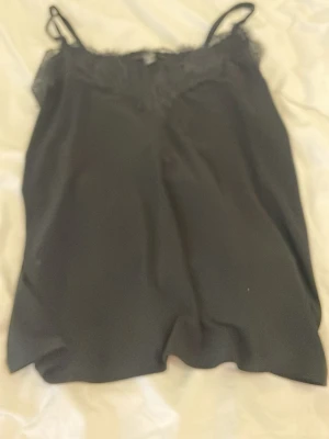 Svart spetsdetaljerad linnetopp Amisu - Tröjan passar mig som har S. Snygg svart linnetopp från Amisu med tunna axelband och spetsdetaljer längs urringningen. Perfekt att styla lager på lager eller bära som den är. Tillverkad i mjukt material som känns skönt mot huden. 