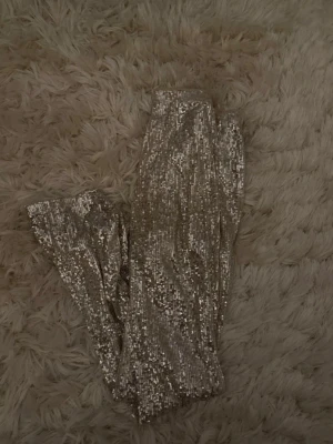 Glittrig  paljettbyxor - Gina Tricot - Snygga utsvängda byxor täckta med silvriga paljetter. Har klippt av lappen för att den kliades men det är strl XS! 
