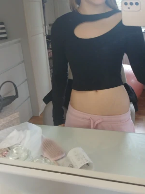 Svart croppad topp med cut out - Trendig svart croppad topp med lång ärm och cool cut out-detalj vid halsen. Sitter tight och har en modern look som passar perfekt till byxor eller kjol. Enkel att styla för en edgy vibe.