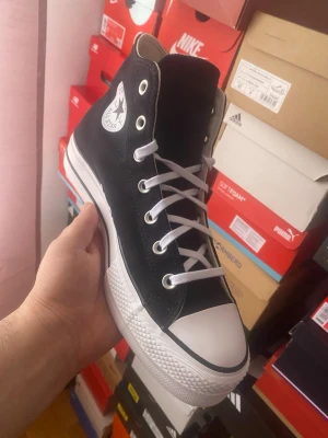 Svarta Converse Chuck Taylor High - Klassiska svarta Converse Chuck Taylor All Star high sneakers med vit tåhätta, vita snören och sula. Ikonisk logga på sidan och metallöljetter. Ovandel i canvas och sula i gummi. Perfekta för en avslappnad och cool stil.