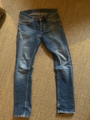 Grim Tim jeans från nudie  - Snygga blåa jeans från nudie, har används ett tag. Jag har lagat dom en gång på nudie och dom sitter fint. Waist är 27 och length är 30. Modell grim tim. Hör av er om ni har några frågor!