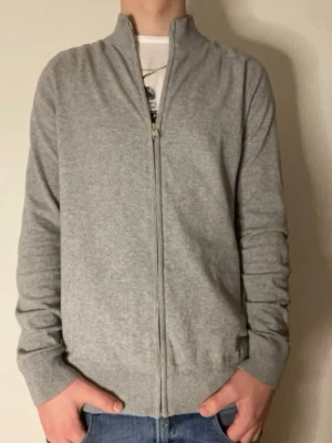 Grå ziptröja från Bruun & Stengade - Snygg grå ziptröja från Bruun & Stengade med hög krage och hel dragkedja framtill. Tröjan har ribbade muddar vid ärmslut och nederkant, perfekt att slänga på sig över en t-shirt. Enkel och stilren design som funkar till det mesta.
