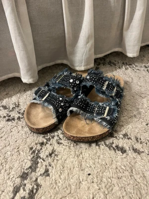 Blå jeans sandaler med nitar - Säljer ett par sandaler med 2 breda remmar i blått jeansmaterial med nitar. Remmar för justering som ger cool streetkänsla foamed innersula och korksula för skön komfort
