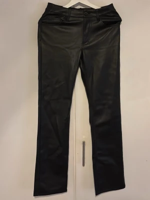 Svarta skinnbyxor med raka ben - Snygga svarta skinnbyxor med raka ben och klassisk femficksdesign. Byxorna har bälteshällor och detaljerade sömmar både fram och bak. Perfekta för en edgy och trendig look.