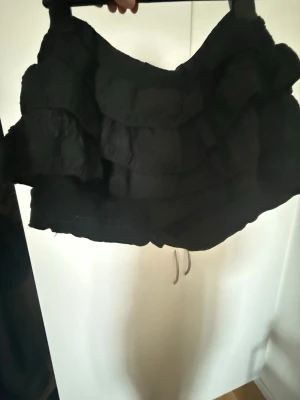 volangkjol  - Supersnygg svart kortkjol med flera volanger. Kjolen har en figurnära passform och inbyggda shorts som inte syns