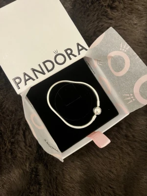 Pandora silverarmband ny skick! - Snyggt silverfärgat armband från Pandora med en rund pärldetalj som lås. Armbandet har en klassisk, tunn och elegant design som passar perfekt till din smyckessamling. Kommer i originalask från Pandora. Aldrig andvänd, fick i present men inte kommit till andvändning därav säljer jag den!