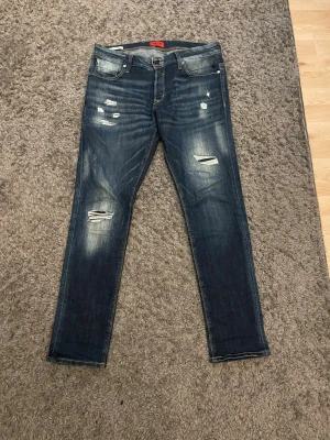 Mörkblå slitna skinny jeans - Säljer ett par mörkblå skinny jeans med slitningar och distressed detaljer på både fram- och baksida. Jeansen har klassisk femficksmodell, låg midja och kontrastsömmar. Perfekta för en avslappnad och trendig look.