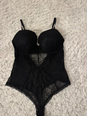 Svart spetsbody med bygel - Snygg svart body i spets i storlek 85C Perfekt för dig som vill ha något som känns både sexigt och trendigt.skulle nog säga att den passar M men allt beror på byst storlek också 