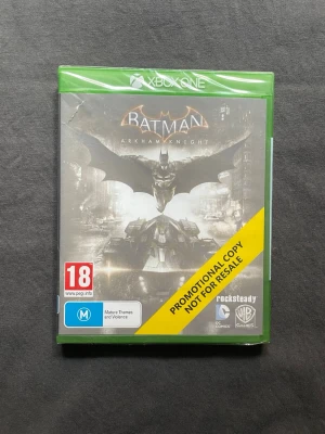 Batman Arkham Knight Xbox One - Promotional Copy (Sealed & New) - Batman Arkham Knight till Xbox One med grön plastfodral. Omslaget har en mörk, dramatisk design med Batman och Batmobilen i centrum. Märkt med "PROMOTIONAL COPY NOT FOR RESALE" och PEGI 18. Perfekt för dig som gillar action och superhjältar.