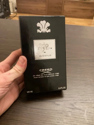 Creed Aventus Eau de Parfum 100 ml - Creed Aventus är en exklusiv parfym med en elegant och lyxig design. Flaskan är transparent med svart och silver detaljer, och kommer i en svart kartong med silver emblem. Parfymen är känd för sin fräscha och kraftfulla doftprofil. 100ml flaska som är näst intill aldrig använd!